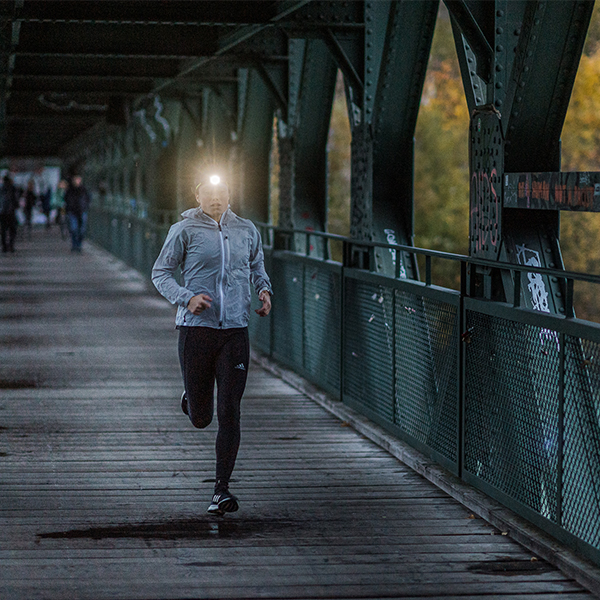 Das Bild zeigt eine Trailrunnerin mit Stirnlampe auf einer Brücke