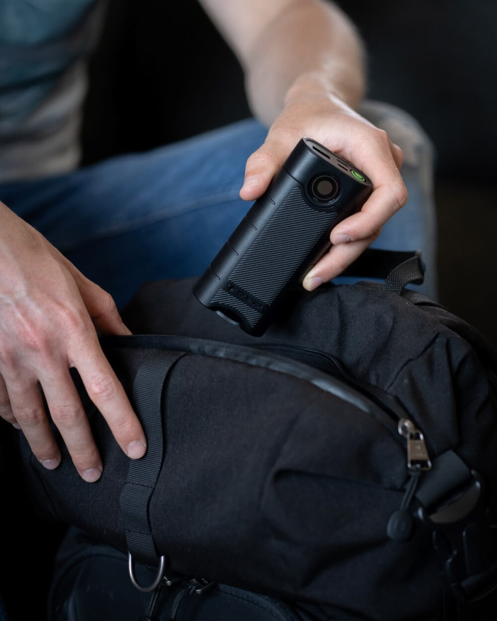 A man is packing his backpack and adds a power bank