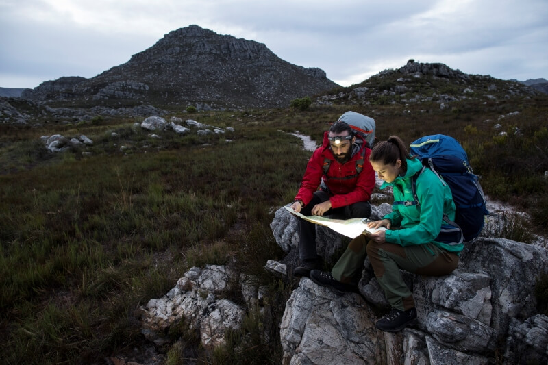 Two people in the mountains are reading a map with headlamps