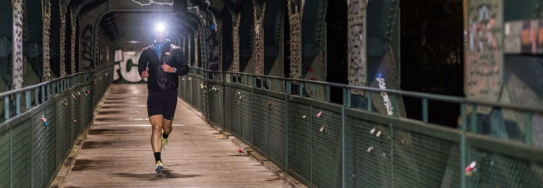 Jogger mit Stirnlampe läuft über eine Brücke