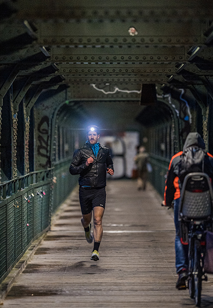 Jogger mit Stirnlampe läuft über eine Brücke