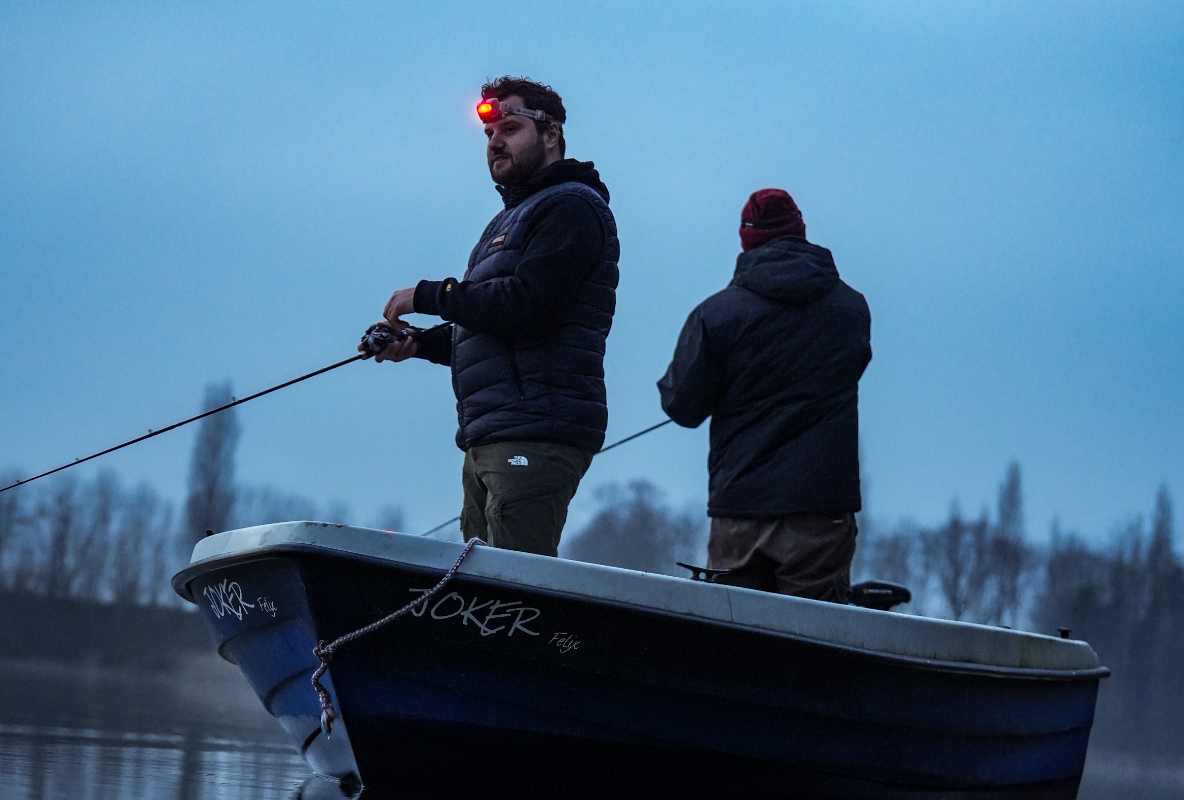Zwei Männer stehen in einem Boot und nutzen eine Stirnlampe mit Rotlicht