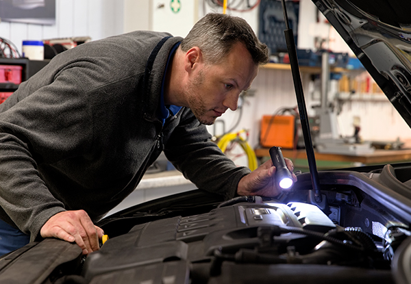 Mechaniker schaut mit einer Taschenlampe unter die Motorhaube eines Autos