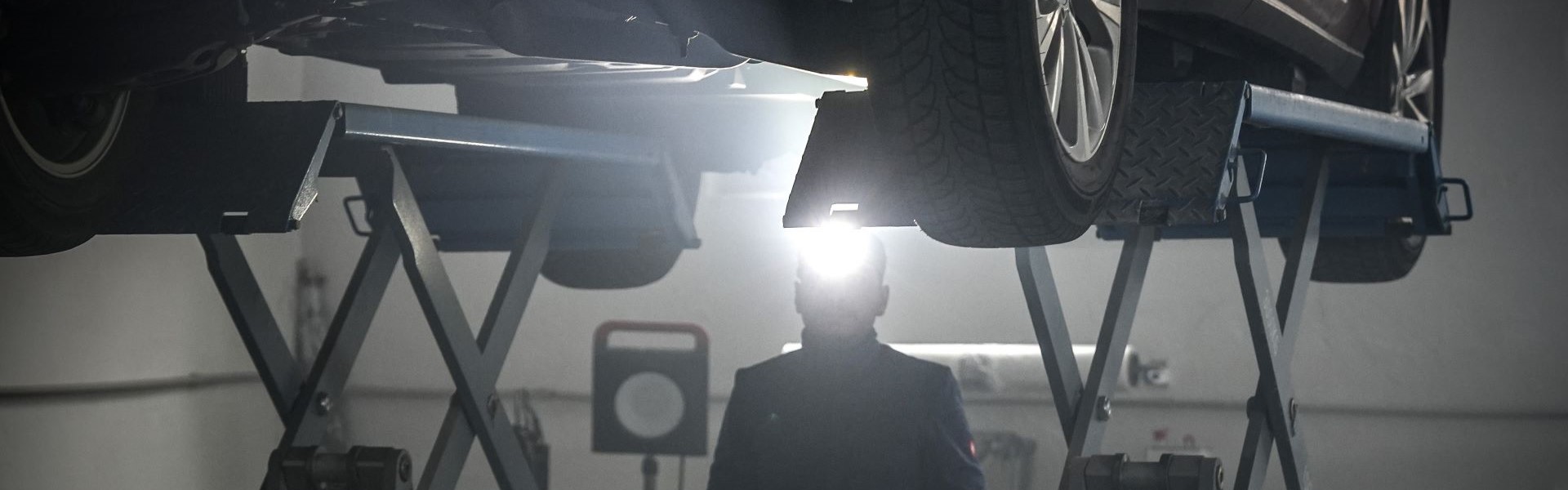 Das Bild zeigt einen Auto-Mechaniker mit Stirnlampe unter einer Hebebühne
