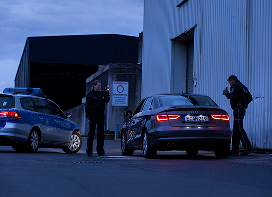 Eine Polizistin und ein Polizist untersuchen im Dunkeln ein Auto mit einer Taschenlampe