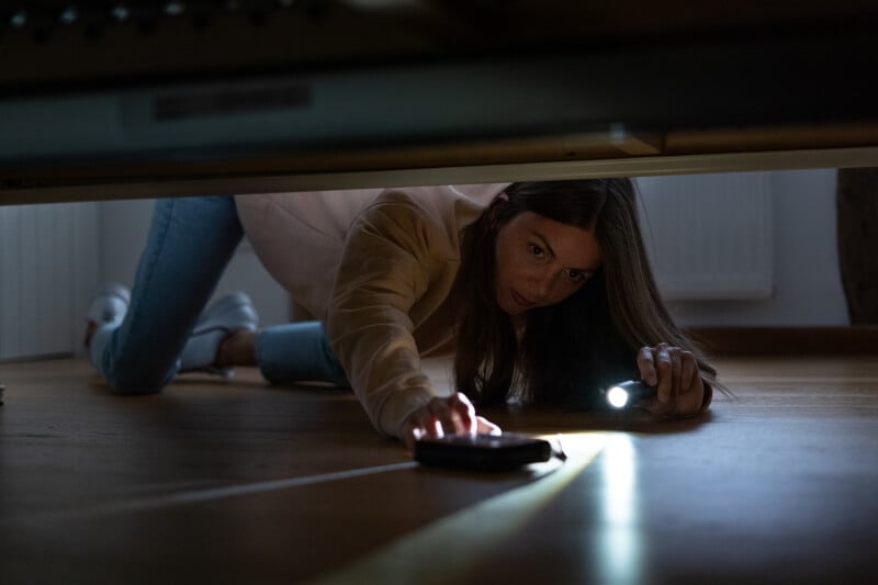 Woman is using a flashlight for searching something under the bed