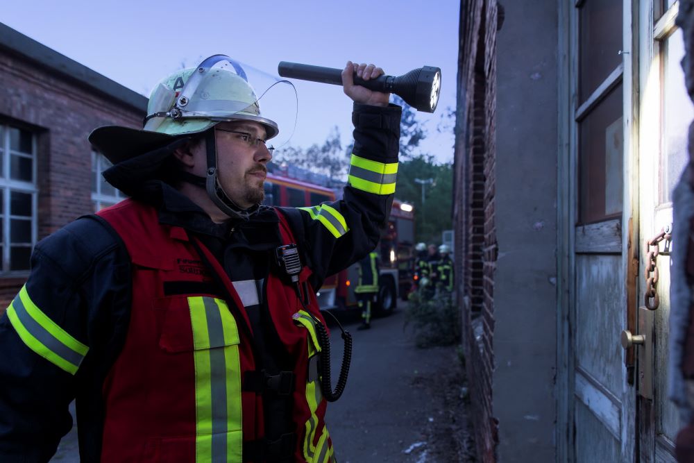 Das Bild zeigt einen Feuerwehrmann mit einer großen Taschenlampe