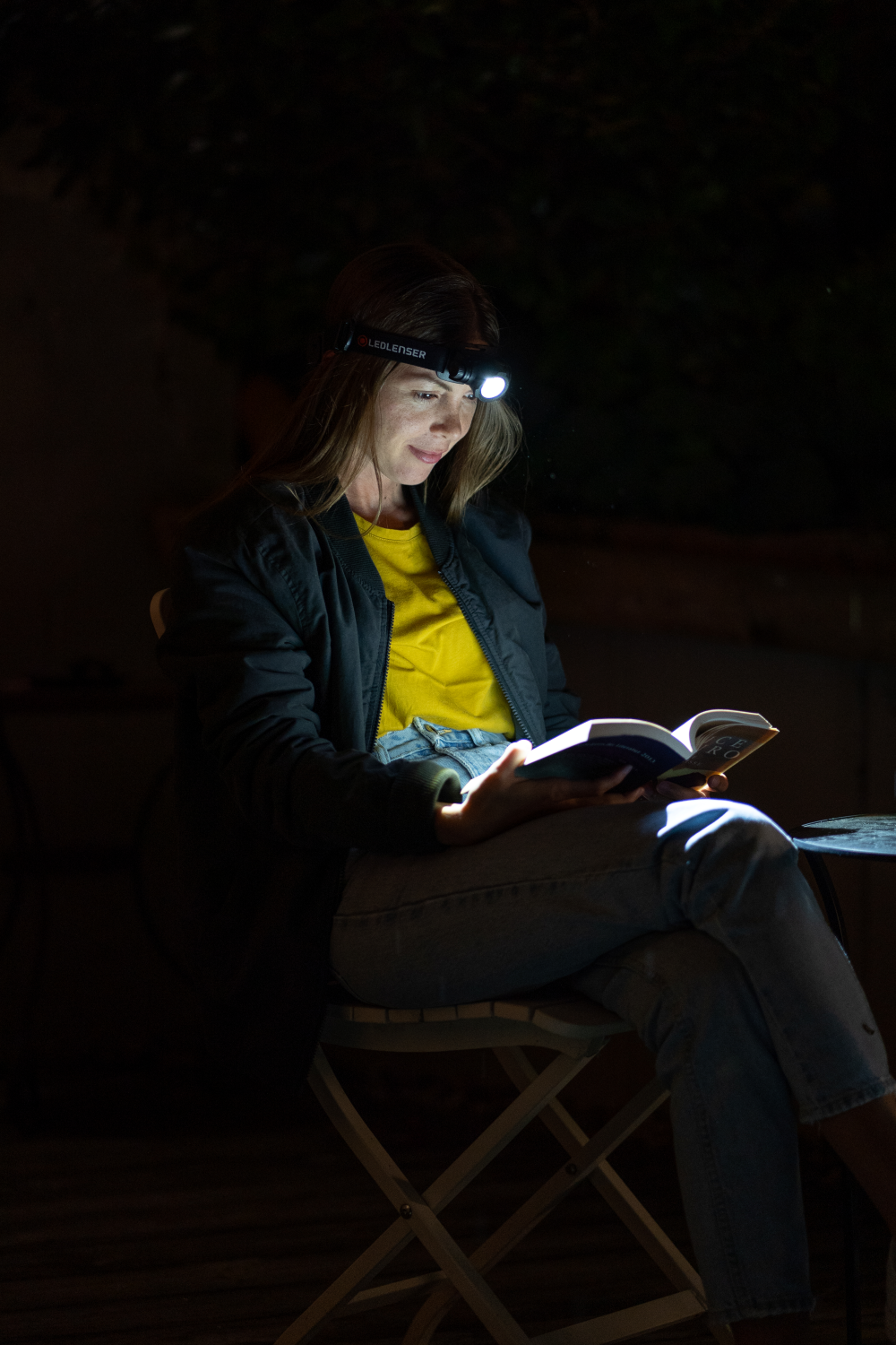 Das Bild zeigt eine Frau, die im Dunkeln mit einer Stirnlampe liest