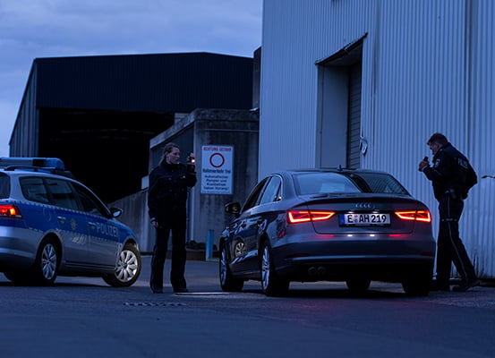 Eine Polizistin und ein Polizist untersuchen im Dunkeln ein Auto mit einer Taschenlampe