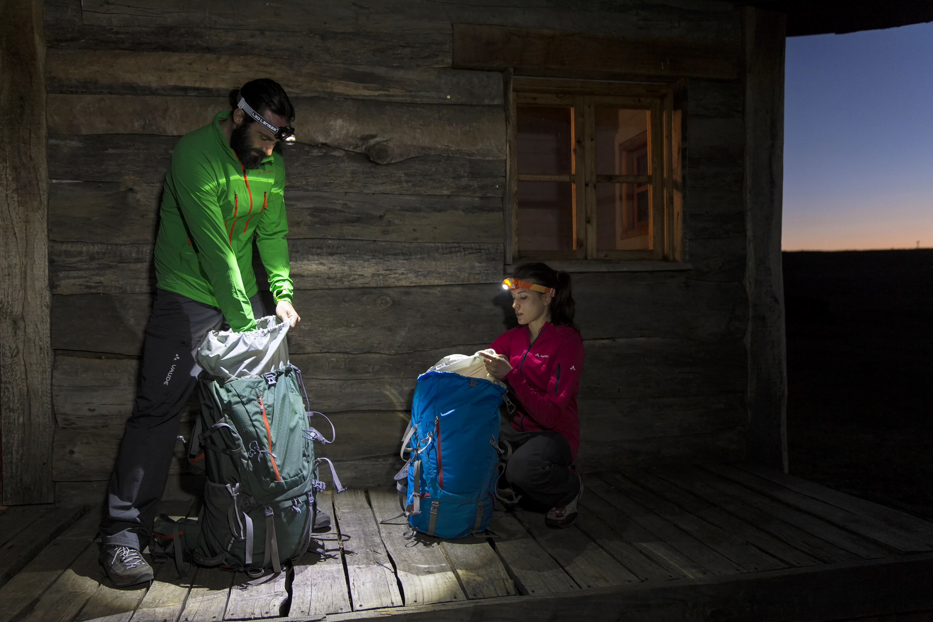 Ein Mann und eine Frau nutzen ihre Ledlenser Stirnlampen, um ihre Rucksäcke zu packen