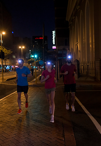 Drei Jogger laufen mit Stirnlampen durch die Stadt