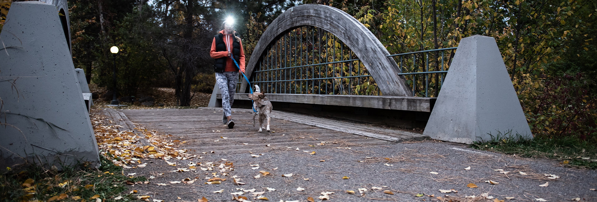 A man with a headlamp is taking his dog for a walk