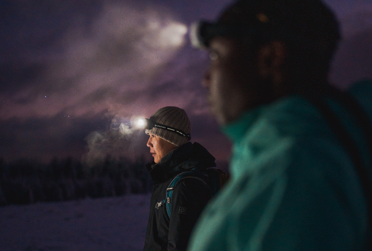 Two people in the snow are using headlamps